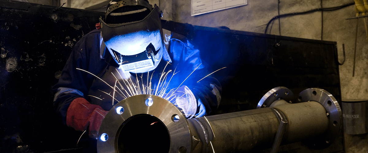 pipefitter welding a pipe wearing full protective equipment in a workshop